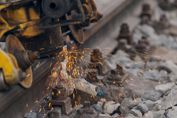 A worker in the process of a railroad track weld repair, reconstruction with a freight train passing