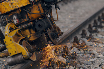 A worker in the process of a railroad track weld repair, reconstruction with a freight train passing