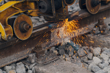 A worker in the process of a railroad track weld repair, reconstruction with a freight train passing