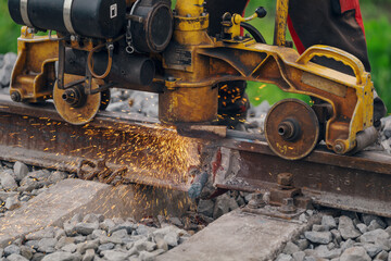 A worker in the process of a railroad track weld repair, reconstruction with a freight train passing