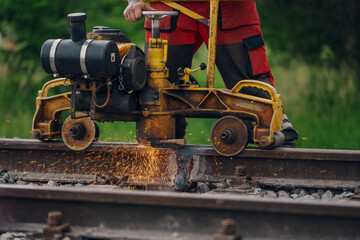 A worker in the process of a railroad track weld repair, reconstruction with a freight train passing