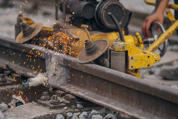 A worker in the process of a railroad track weld repair, reconstruction with a freight train passing