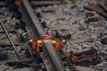 A worker in the process of a railroad track weld repair, reconstruction with a freight train passing
