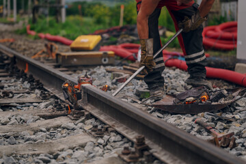 A worker in the process of a railroad track weld repair, reconstruction with a freight train passing