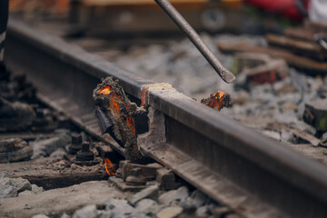 A worker in the process of a railroad track weld repair, reconstruction with a freight train passing