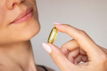 Young beautiful woman holding omega 3 capsule close-up. Biological supplement for beauty, health...