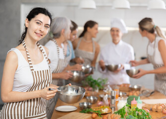 Young woman in apron learning to cook at cooking master class
