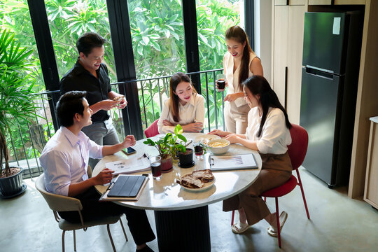 Asian Business Team Meeting Collaboration at Round Table with Food and Drinks Adult Men and Women Discussing Strategy and Ideas in Modern Office Space - Powered by Adobe