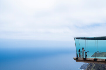 A group of people are looking out over the ocean from a glass-walled observation deck. The view is breathtaking and the people are enjoying the experience