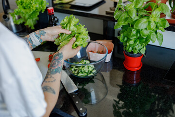 In a bright kitchen, a skilled cook is preparing fresh basil and colorful veggies for a delicious...