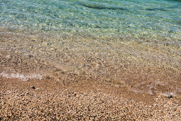Clear water on pebble shore. Coastal texture, summer serenity, and natural detail of Mediterranean beach environment.