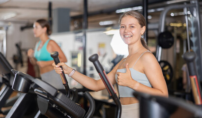 Fototapeta premium Young woman in sportswear training on elliptical machine in gym