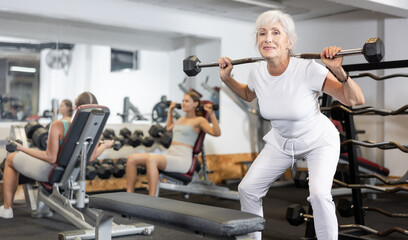 Mature sportswoman doing exercises with a barbell and dumbbells in the gym