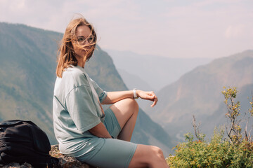 Young woman in sportswear sits on a rock ledge, peacefully observing scenic mountain landscape...