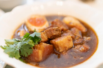 Delicious bowl of savory pork stew with eggs and fresh herbs garnishing.