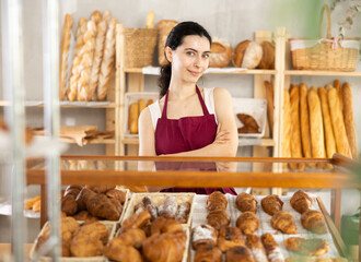 Young woman seller in apron at counter with pastries in bakery