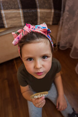 Little girl wearing a pink headband, sitting on the floor of her cozy bedroom, holding a wooden comb and looking up with curiosity and joy, embodying childhood innocence and playfulness