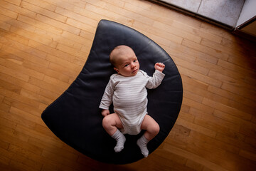 Newborn baby lying comfortably on a crescent-shaped black cushion. The wooden floor adds warmth to the scene, highlighting the baby's peaceful expression and cozy outfit
