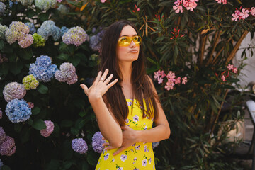 Brunette long hair woman wave her hand because of hot weather, warm summer day, pout lips. Girl wear yellow dress and sunglasses. 