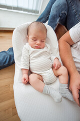 Adorable newborn baby sleeping peacefully in a podster, a safe and comfortable place for infants, with father's legs visible in the background, providing a sense of security and love
