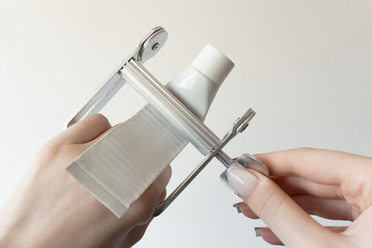 Metal tube squeezer with a white cosmetic or toothpaste tube inserted, held in two hands on a light background. Perfect for concepts of minimalism, hygiene, eco-friendly consumption.