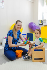 Pediatric play therapy. Female physiotherapist doing physical therapy on a child focusing on play activities for concentration and attention