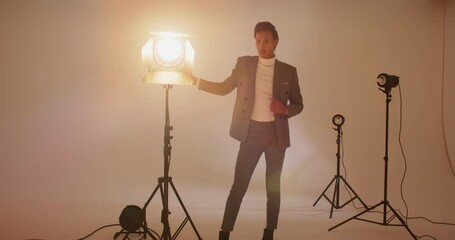 Asian male model entering frame adjusting suit rotating spotlight stand in studio for photoshoot - Powered by Adobe