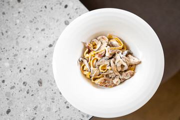 A bowl of creamy pasta with mushrooms and chicken, served on a speckled countertop. The dish is appetizing, rich in texture, and perfect for culinary content or food photography.