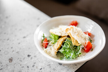 Fresh Caesar salad with crisp lettuce, crunchy croutons, grated Parmesan, sliced tomatoes, and creamy dressing, served in a white bowl on a speckled countertop.