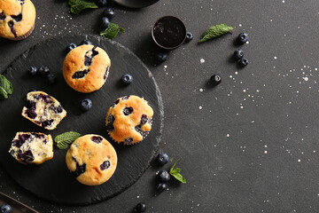 Stone tray with tasty blueberry muffins on black background