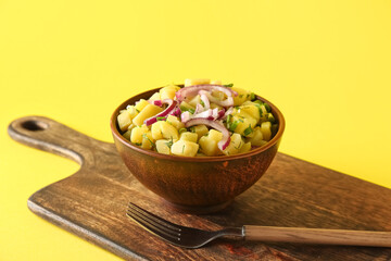 Bowl of tasty potato salad with onion on yellow background