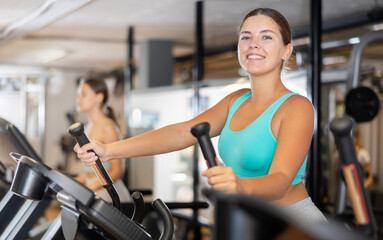 Fototapeta premium Young athletic woman working out on elliptical machine in gym