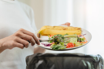 Compost from leftover food in the meal in household, female hand holding left over meal use fork scraping waste, rotten vegetable throwing away into garbage, trash or bin. Environmentally responsible