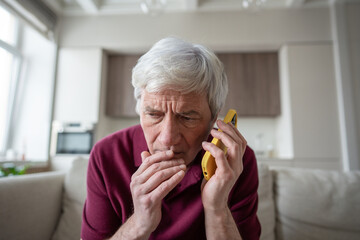 Distrustful and suspicious senior man frowns during emergency call, listening to pressured demands...