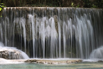Experience the natural beauty of a flowing waterfall cascading over rocks in a lush green forest park, Kouangsi waterfall Luang Prabang