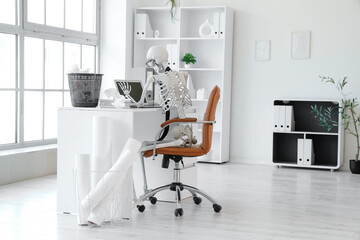Human skeleton model with laptop on desk in office