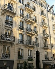 Obraz premium Elegant Parisian apartment building with ornate balconies, cream walls, and a charming storefront at street level.