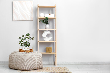 Fototapeta premium Interior of stylish room with shelving unit and beautiful eucalyptus branches on pouf