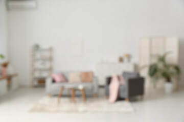 Blurred view of living room with comfortable sofa, armchair and table near white wall