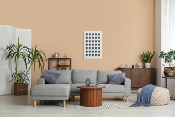 Comfortable sofa, table and pouf near beige wall in interior of living room