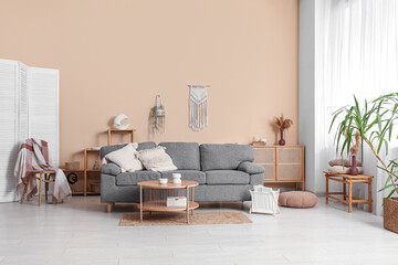 Comfortable sofa, table and magazine holder near beige wall in interior of living room