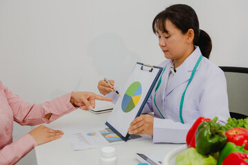 An Asian female nutritionist attentively discusses dietary habits with a patient, offering...