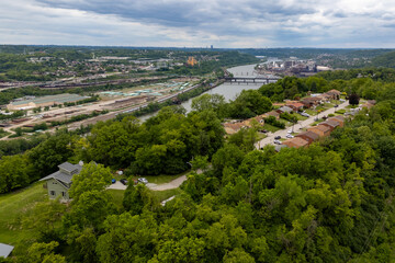 Cityscape from hilltop: urban buildings under blue sky, sprawling roads, and people in the distance.