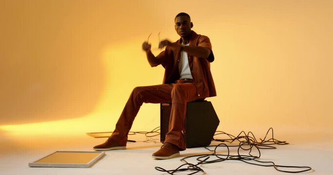 In studio African American man sitting on speaker unbuttoning shirt to reveal tank top, walking off
