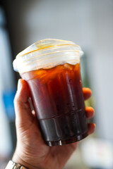 Cropped short view of someone hand holding a plastic cup of iced black coffee.