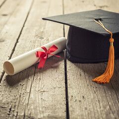 Graduation hat and diploma on wooden table with soft shadows