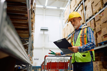Senior worker analyzing paperwork while checking inventory on shelves at distribution warehouse.