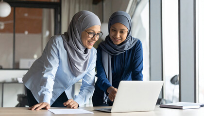Two Happy Muslim Female Employees Collaborating in Modern Office Environment