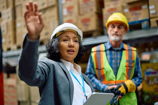 Mature female inspector visiting workers at distribution warehouse.