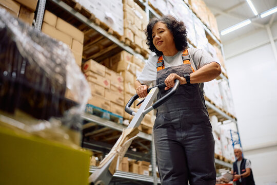 Below view of female warehouse worker pushing packages on pallet jack. - Powered by Adobe